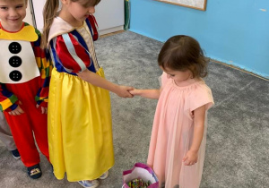 3 urodziny Amelki. Dziewczynka składa Amelce życzenia, podaje rękę. Na dywanie stoi torebka z cukierkami. Za dziewczynką stoi chłopiec.